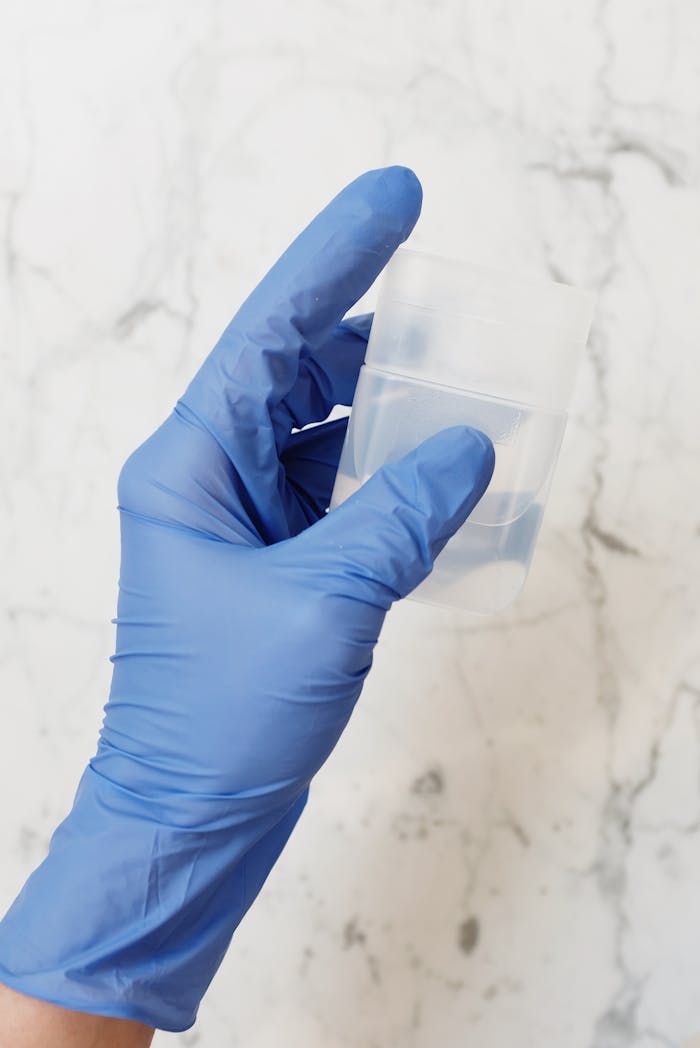 A blue-gloved hand holding a clear medical container in a sterile indoor environment.